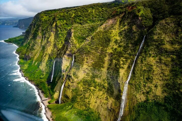 Aerial of lush Hamakua Coast sea cliffs with waterfalls cascading into the blue ocean, Big Island.