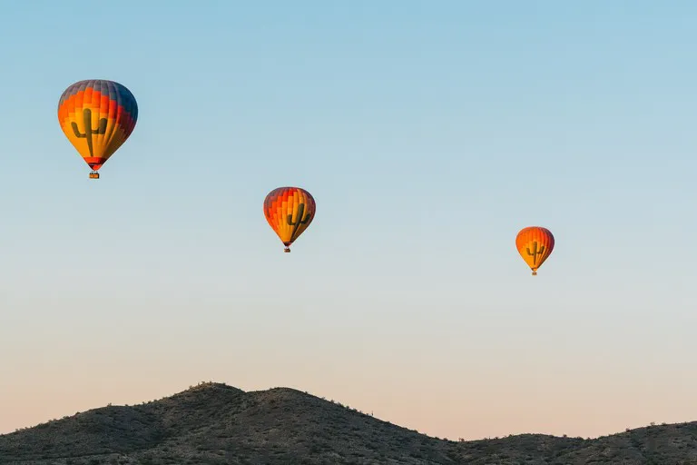 Three orange-red hot air balloons over a desert ridge at golden hour near Phoenix.