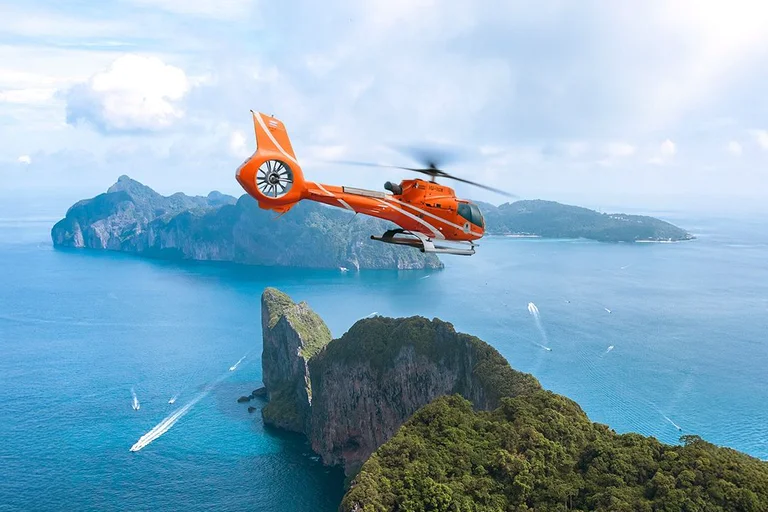 An orange helicopter flying over turquoise sea and limestone cliffs in the Phi Phi islands