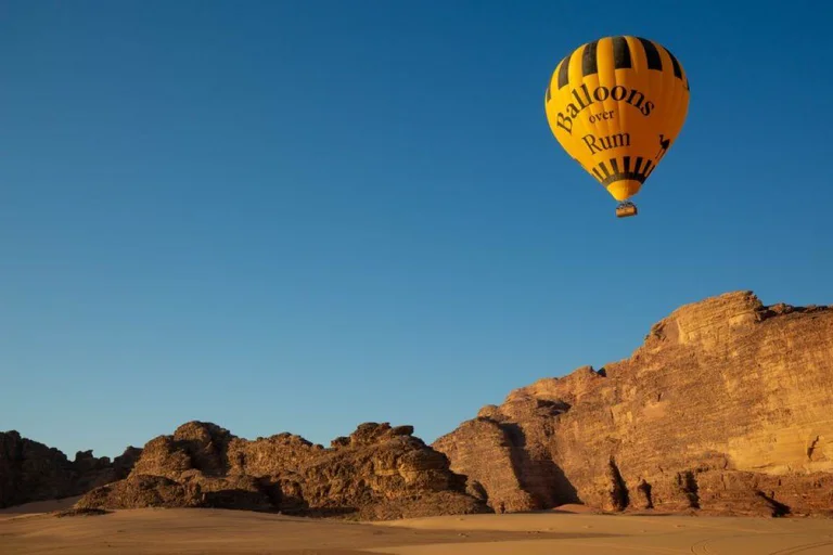 Yellow and black hot air balloon high in a deep-blue sky above the sandstone cliffs and sand of Wadi Rum